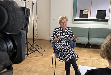 Volksanwältin Gaby Schwarz sitzt auf einem Stuhl in ihrem Büro und gibt ein TV Interview.